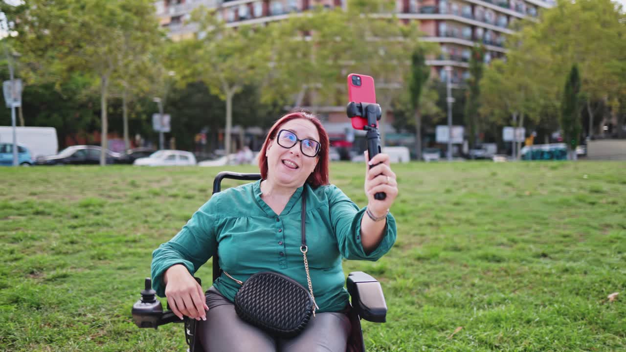 Glückliche Frau im Elektrorollstuhl vloggt mit Smartphone im Park