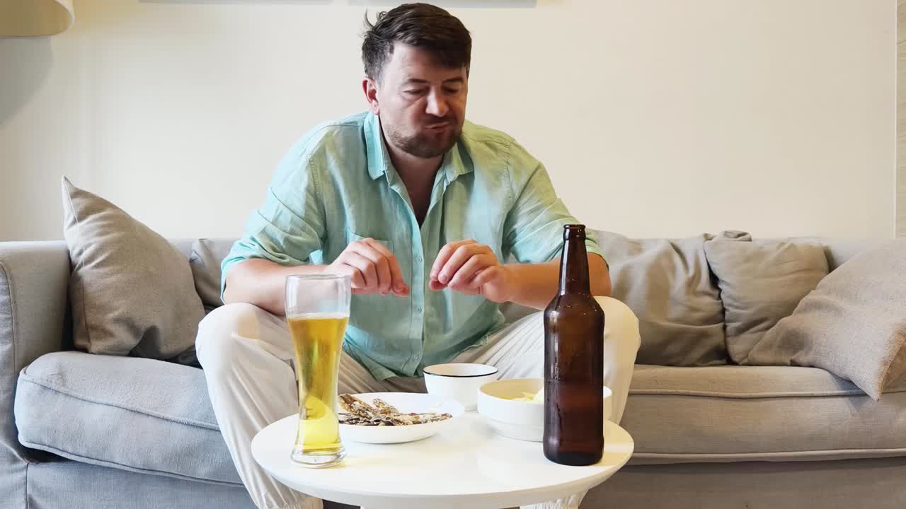 Man eating dried fish and drinking beer on sofa