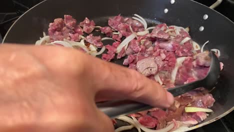 Unrecognizable-hand-cooking-meat-with-onions