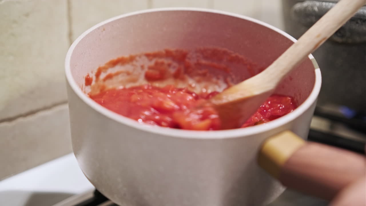 mezclar salsa de tomate con cuchara de madera mientras se cocina en la estufa - primer plano, tiro estático
