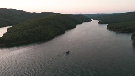 Aerial-view-of-small-boat-on-Albanian-river-and-forest-hillside-aside