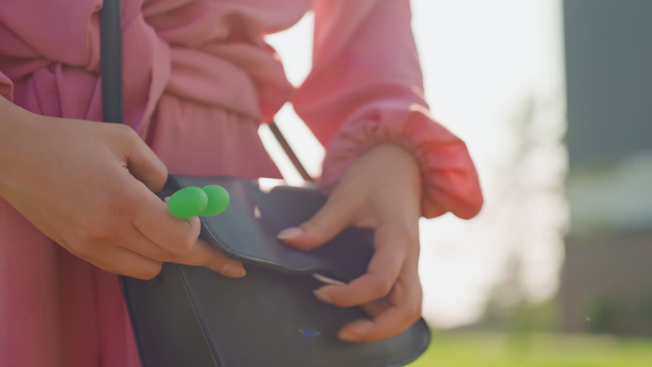 Person Retrieves Toy Outdoors, Woman In Pink Dress Takes Fidget Toy From Stylish Bag Outside, Young Lady With Pink Sleeves Retrieves Silicone Fidget Toy From Her Purse On Casual Sunny Street