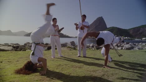 group practicing capoeira outdoors by the water with scenic views