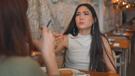 dos mujeres compartiendo postre y probando comida en un café