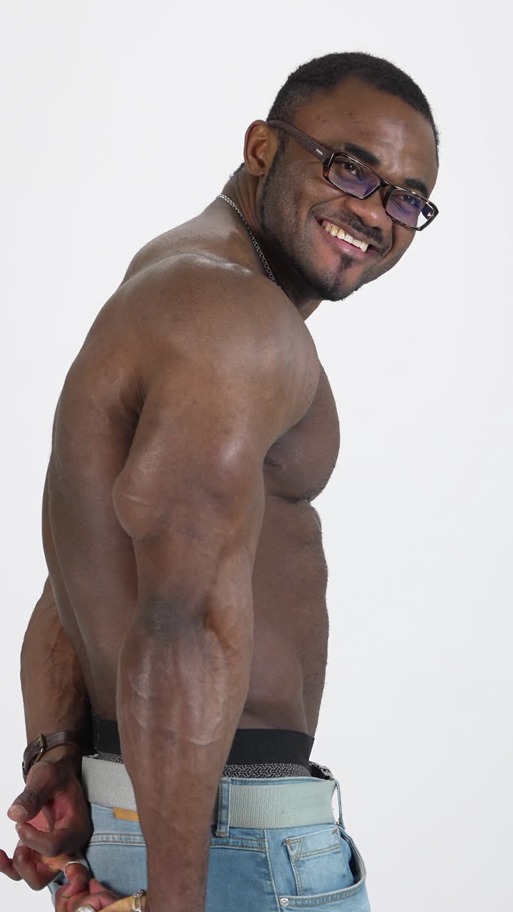 Muscular afro american guy in studio. Shirtless sportsman with black skin posing on camera on white background. Smiling athlete with sportive body. Vertical video