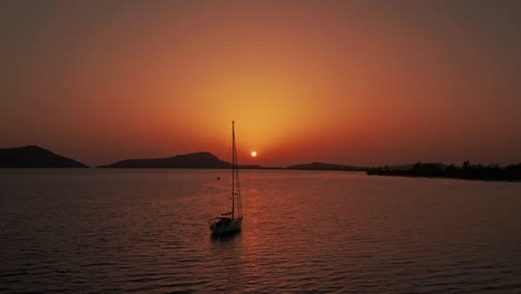 órbita-Aérea-Alrededor-De-Un-Velero-Anclado-En-Mar-Abierto-Frente-A-La-Costa-De-Pylos-Grecia,-Cielo-Al-Atardecer