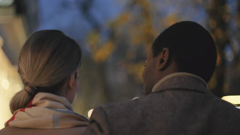 rear of a romantic couple hugging and walking in the street at night