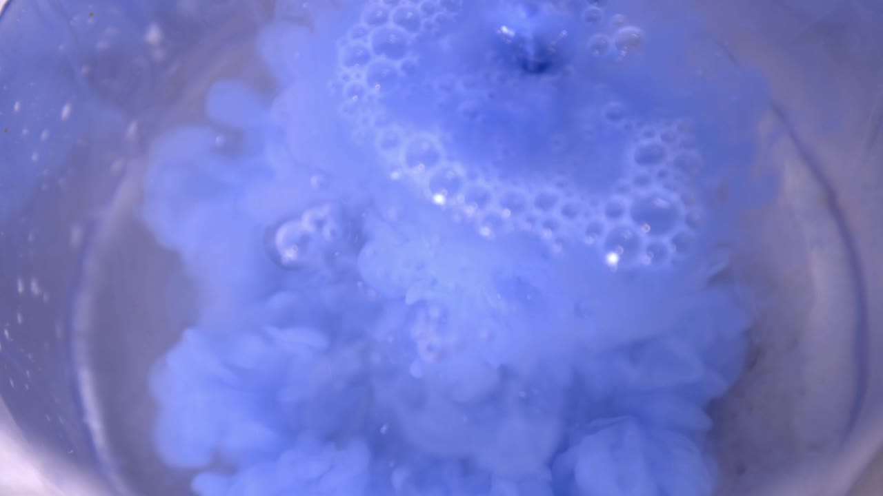 Pouring Sky Blue Liquid Paint Into A Glass Of Clear Water - Low-Angle Shot