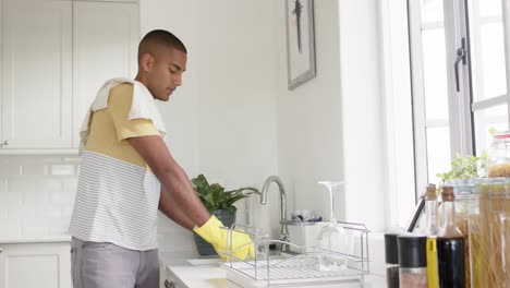 hombre biracial lavando platos en una cocina brillante, cámara lenta