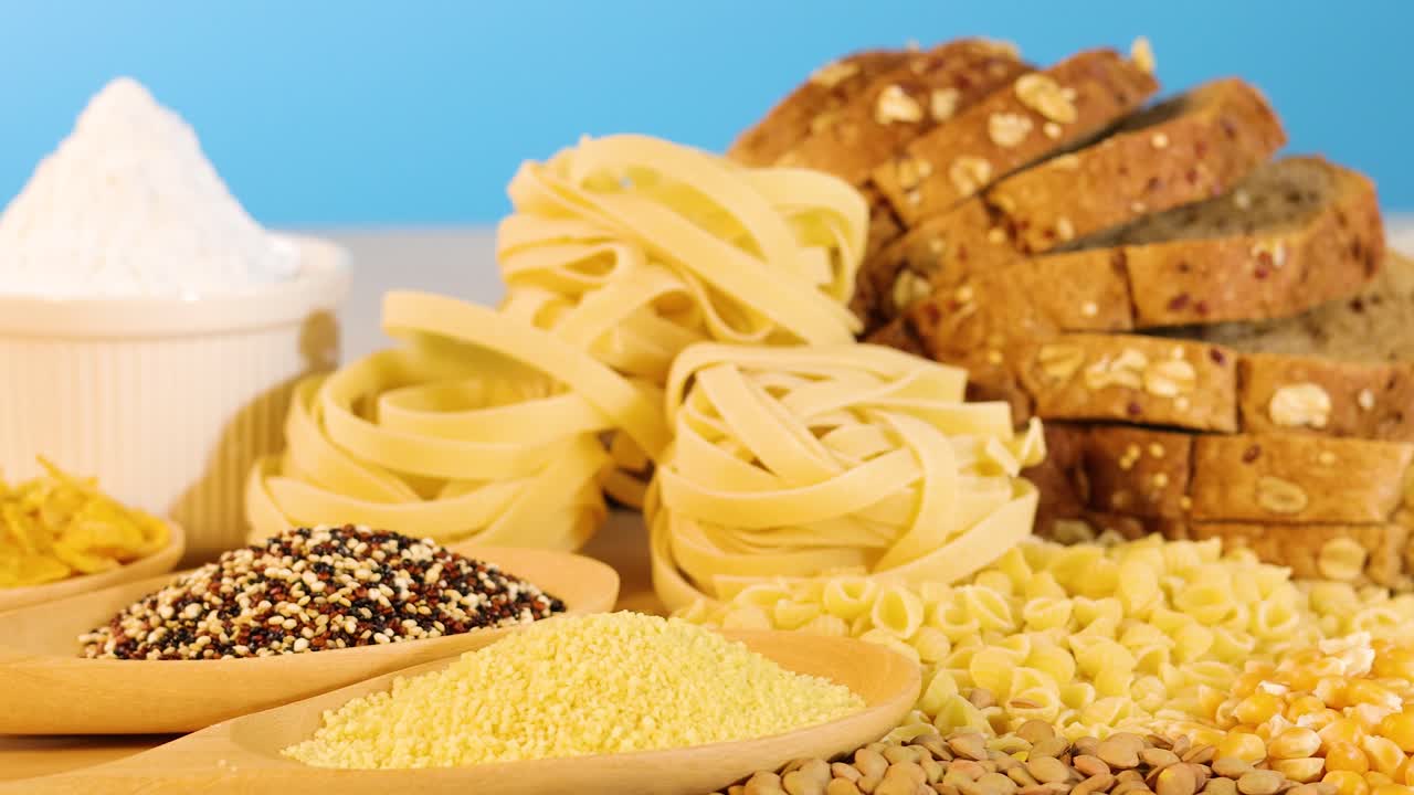 A variety of grains, pasta, and bread arranged against a bright blue backdrop, highlighting textures and colors