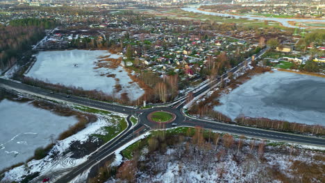 lago congelado al lado de una carretera con rotonda, principios del invierno, casas en el fondo, vista aérea