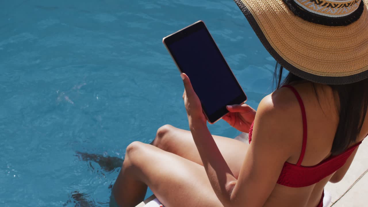 mujer de raza mixta sentada junto a una piscina en casa