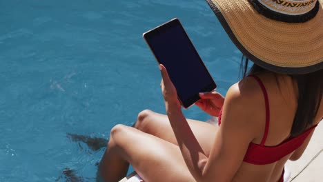 mujer de raza mixta sentada junto a una piscina en casa