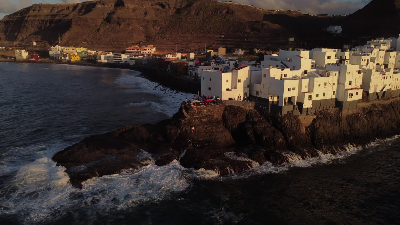 playa de san andrés en arucas: vista aérea con movimiento en la distancia a los edificios blancos en la playa de san andrés y las olas que golpean la costa