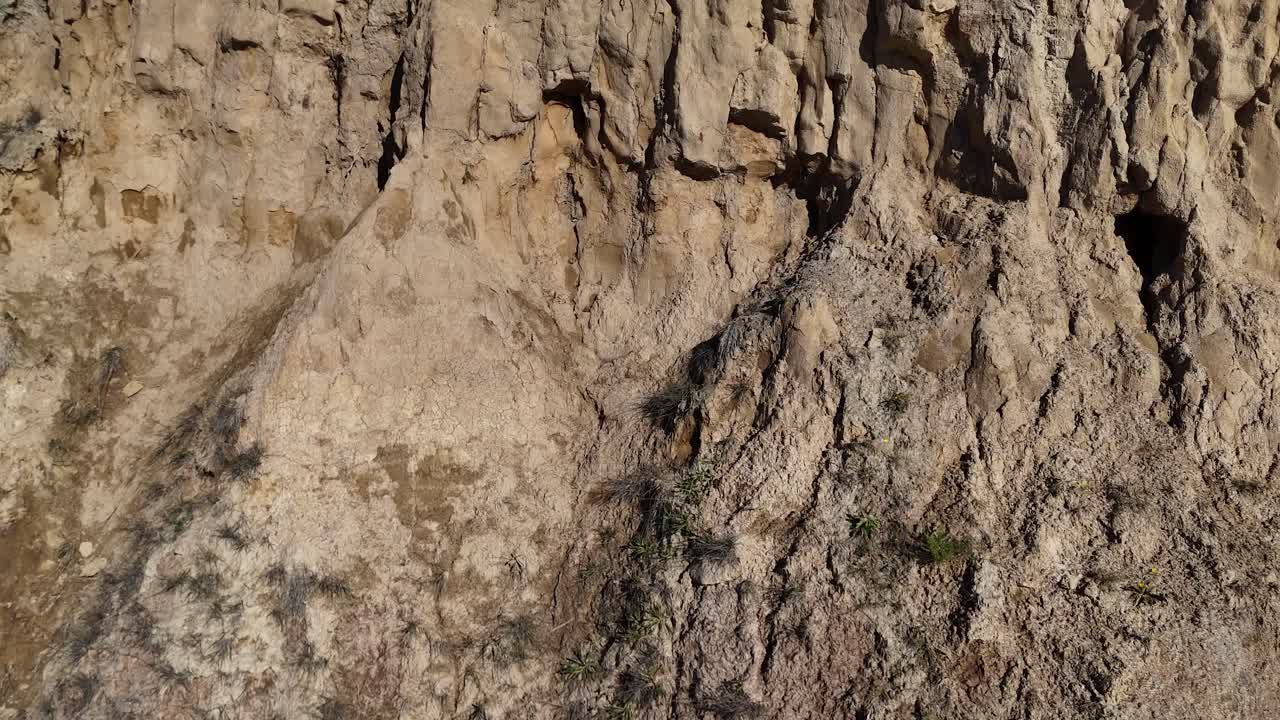 Aerial footage showcasing detailed sandstone cliff textures in Akaroa, New Zealand, with visible soil and sparse vegetation