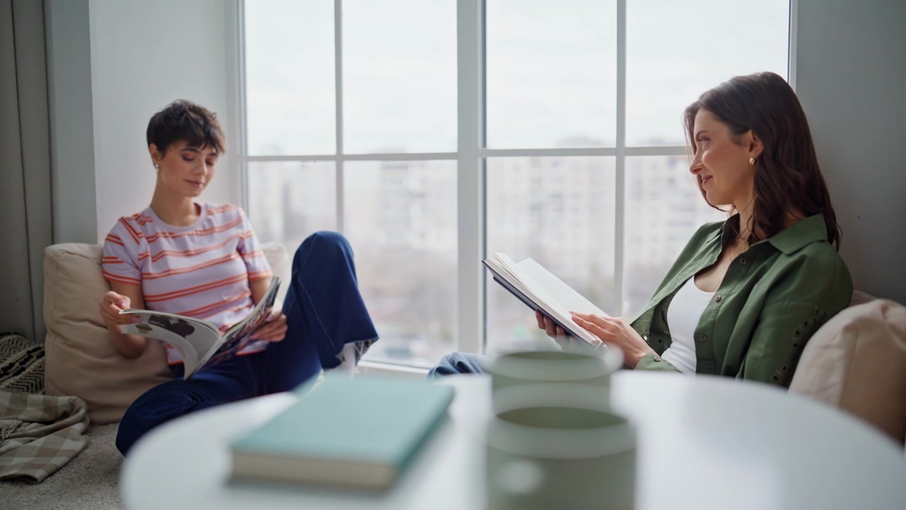 Due donne leggono insieme sedute in appartamento. Coppia di ragazze immerse nella letteratura.