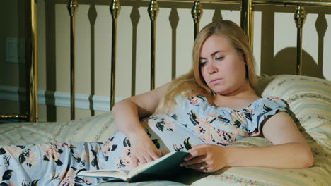 young pregnant woman is relaxing in her bedroom reading a book