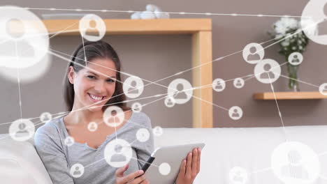 Animation-of-network-of-connections-with-icons-over-caucasian-woman-using-tablet