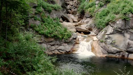 Un-Puente-Cubierto-Cruza-Un-Desfiladero-Sobre-Un-Arroyo-Rocoso-Rodeado-De-Bosque-Mientras-La-Cámara-Se-Inclina