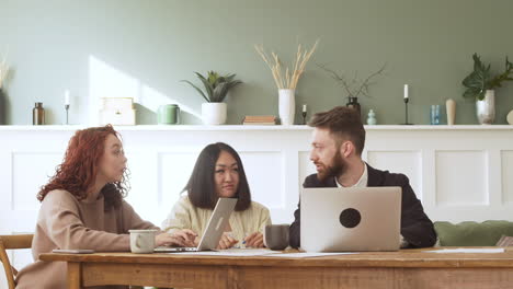 group of three multiethnic colleagues sitting at table and debating while looking laptop computer