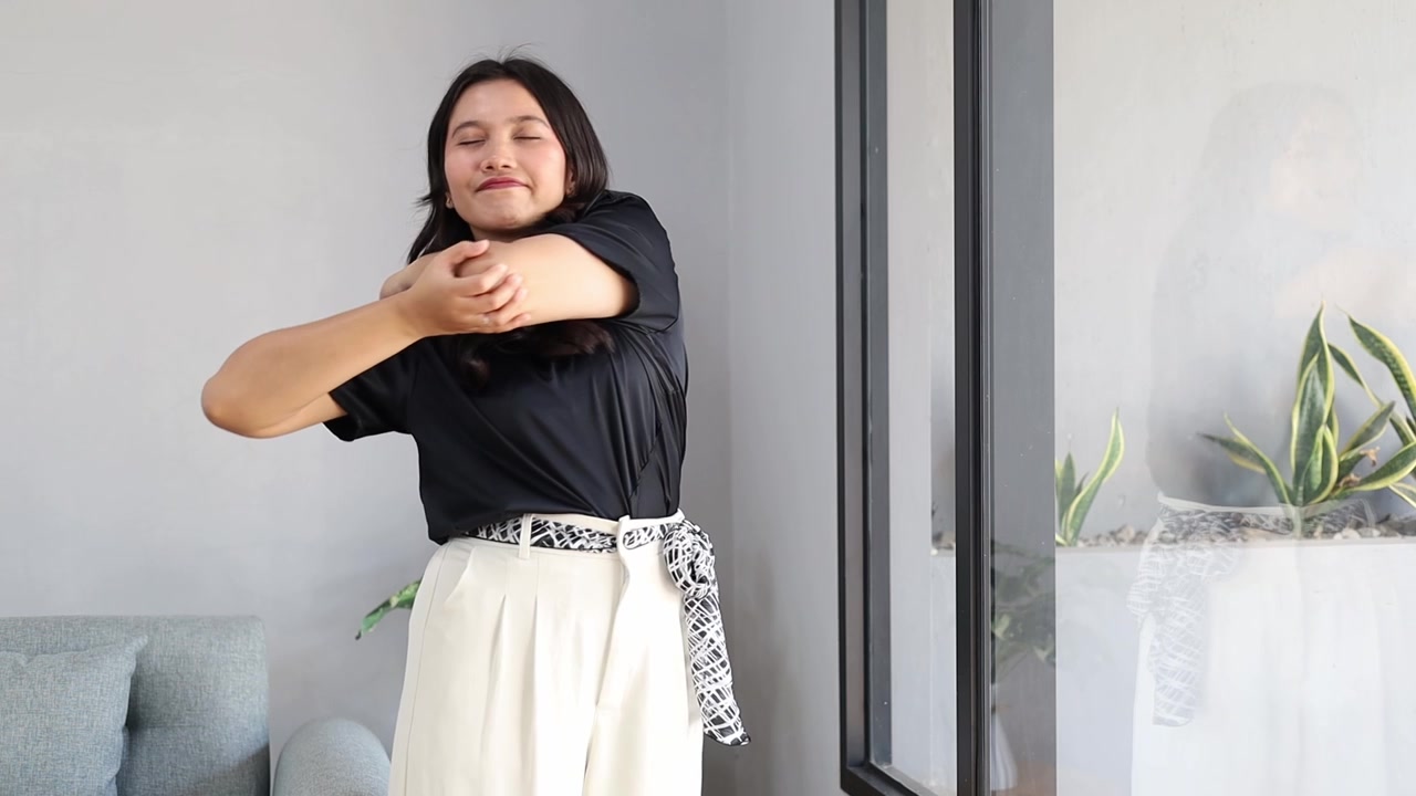 Jovem e atraente mulher asiática alongando os braços e aproveitando a luz do sol da manhã em casa