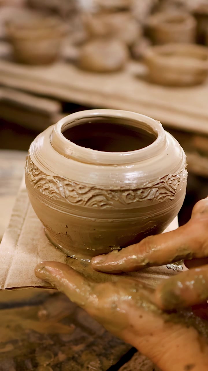 Primo piano di mani infangate che sollevano un vaso di ceramica dettagliato da un tornio da vasaio.
