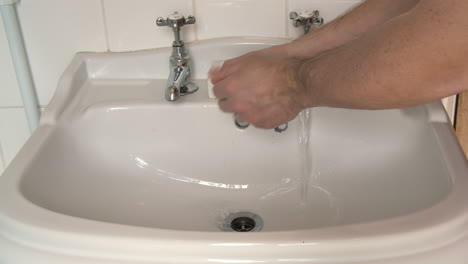 male hands wash and scrub with soap for twenty seconds in a white bathroom sink