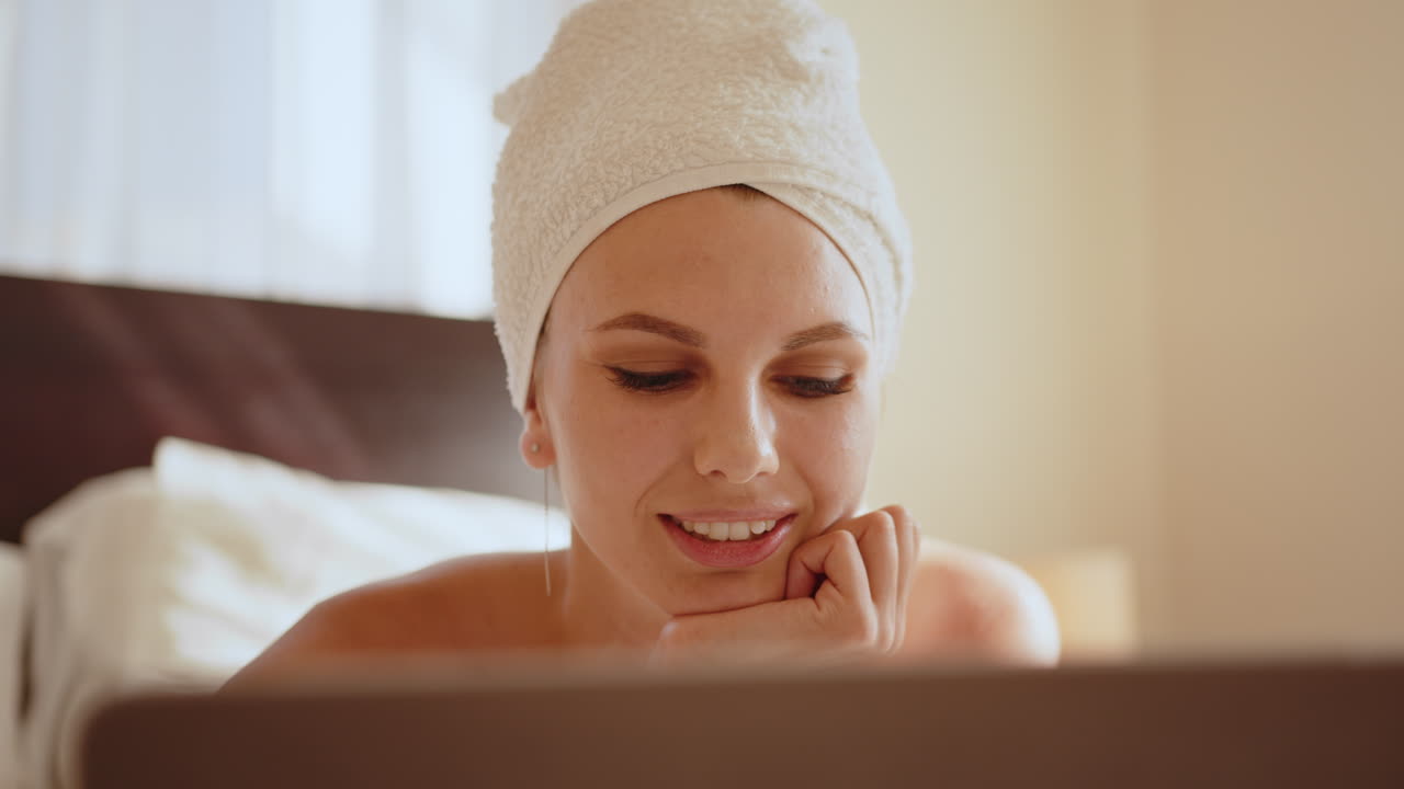 Donna che si rilassa a letto con un asciugamano in testa e usa un laptop