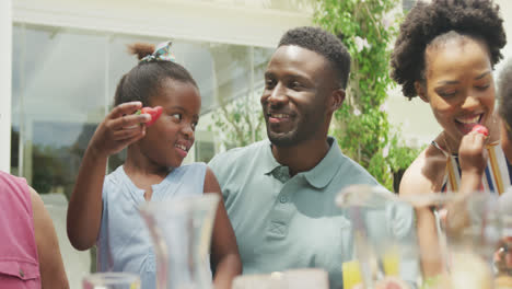 Happy-african-american-family-talking-and-having-breakfast-in-garden