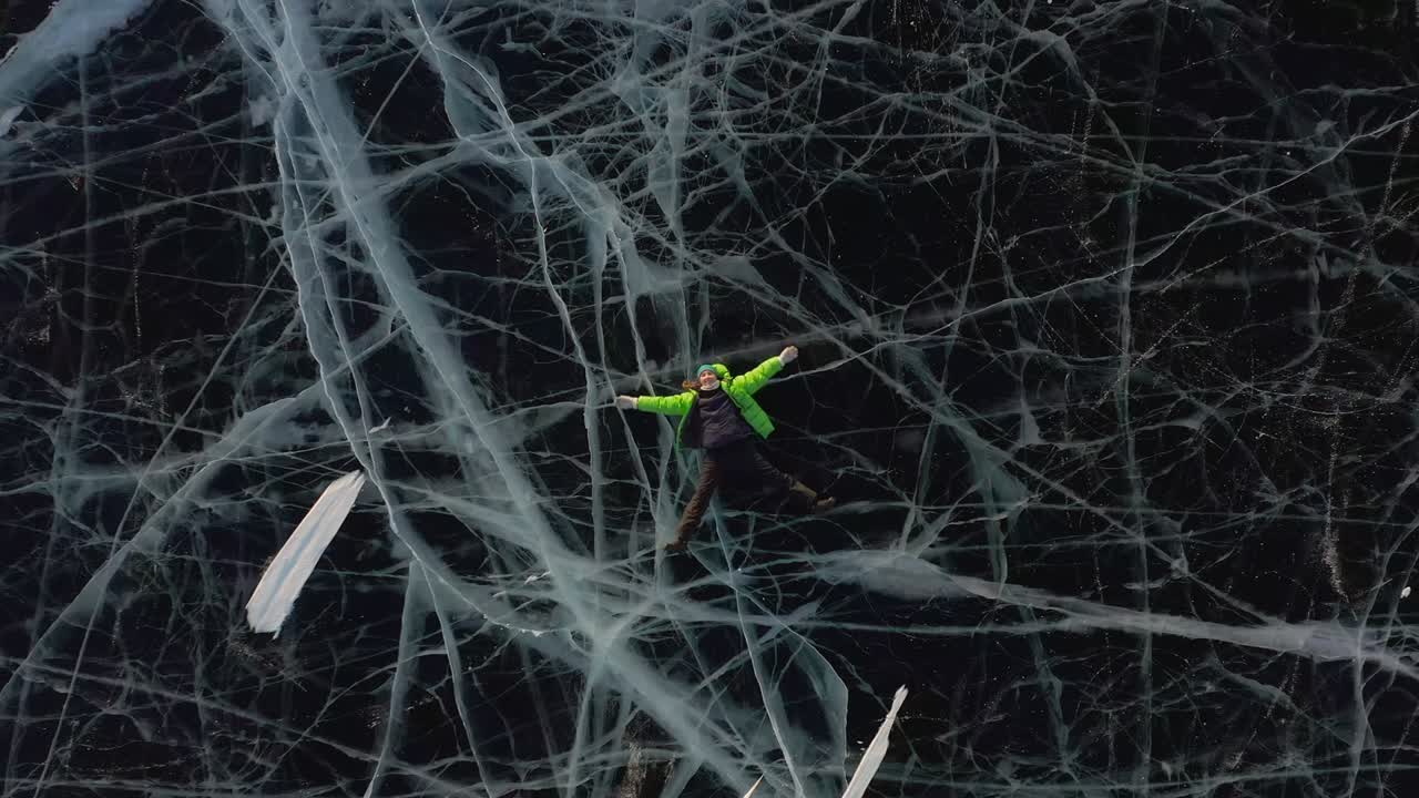 una chica yace en el hielo en invierno con ropa cálida y agitando sus brazos y piernas