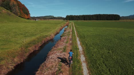 one young woman cycling with a touring bike in a green field in autumn nature in bavaria