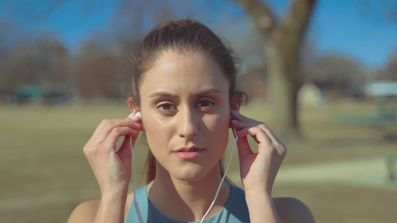 retrato de una linda chica fitness poniéndose los auriculares antes de hacer ejercicio mirando la cámara con confianza, primer plano