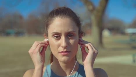 portrait of pretty fitness girl putting on earphones before work out looking at camera with confidence, close up shot