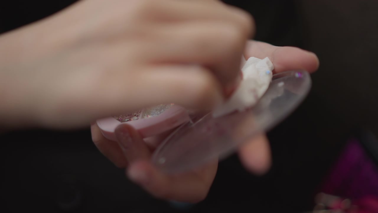 Close-up view of hands pressing, rubbing, and lifting white cosmetic powder inside small round compact with clear lid open, showing careful beauty application, product handling, soft texture, and