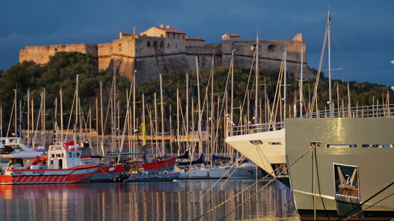 Båtar som ligger i hamnen i Port Vauban med Fort Carre i bakgrunden vid solnedgången i Antibes, Frankrike