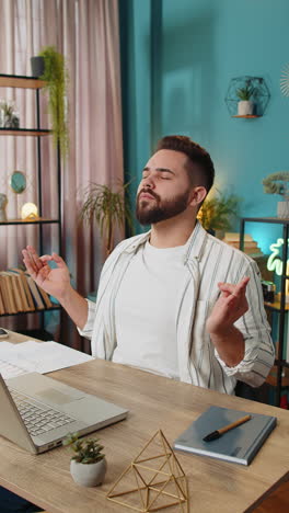 peaceful relaxed businessman sitting at workplace with folded in mudra gesture hands meditating