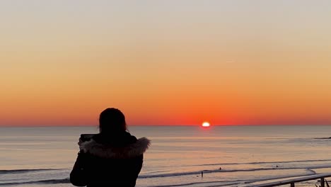 silhouette of young woman takes a picture from phone on the beach at huge sunset