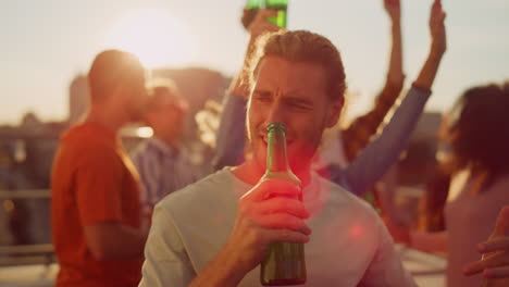 cheerful man drinking beer at rooftop party. happy guy dancing outdoors.