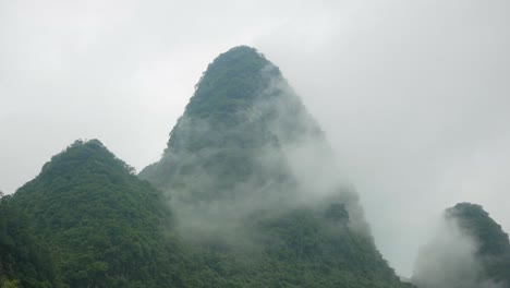 Cruising on a boat along a brown river in Guilin, China. Watching the foggy green mountains in the background
