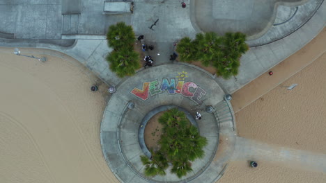 Antena:-Vista-De-Pájaro-Del-Hombre-Parado-En-El-Cartel-De-Venecia-En-El-Parque-De-Patinaje,-Los-Ángeles,-California-Nublado