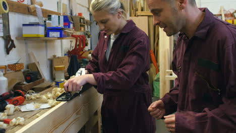 carpenter with female apprentice planing wood in workshop