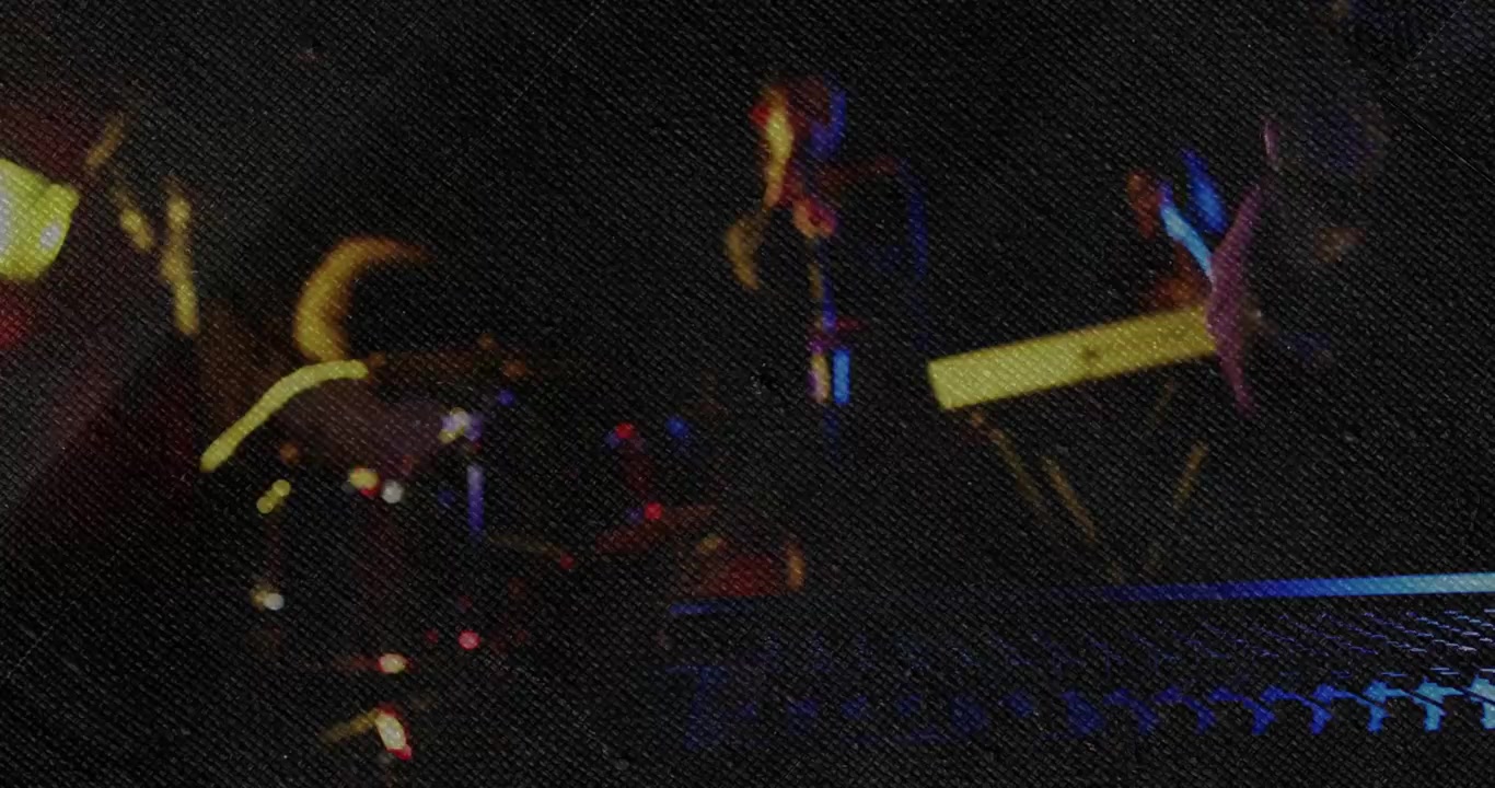 Sanger i bevægelse synger sang i mikrofon, mens lysstråle rammer klub, trommer og keyboards spiller, iført mørkt tøj