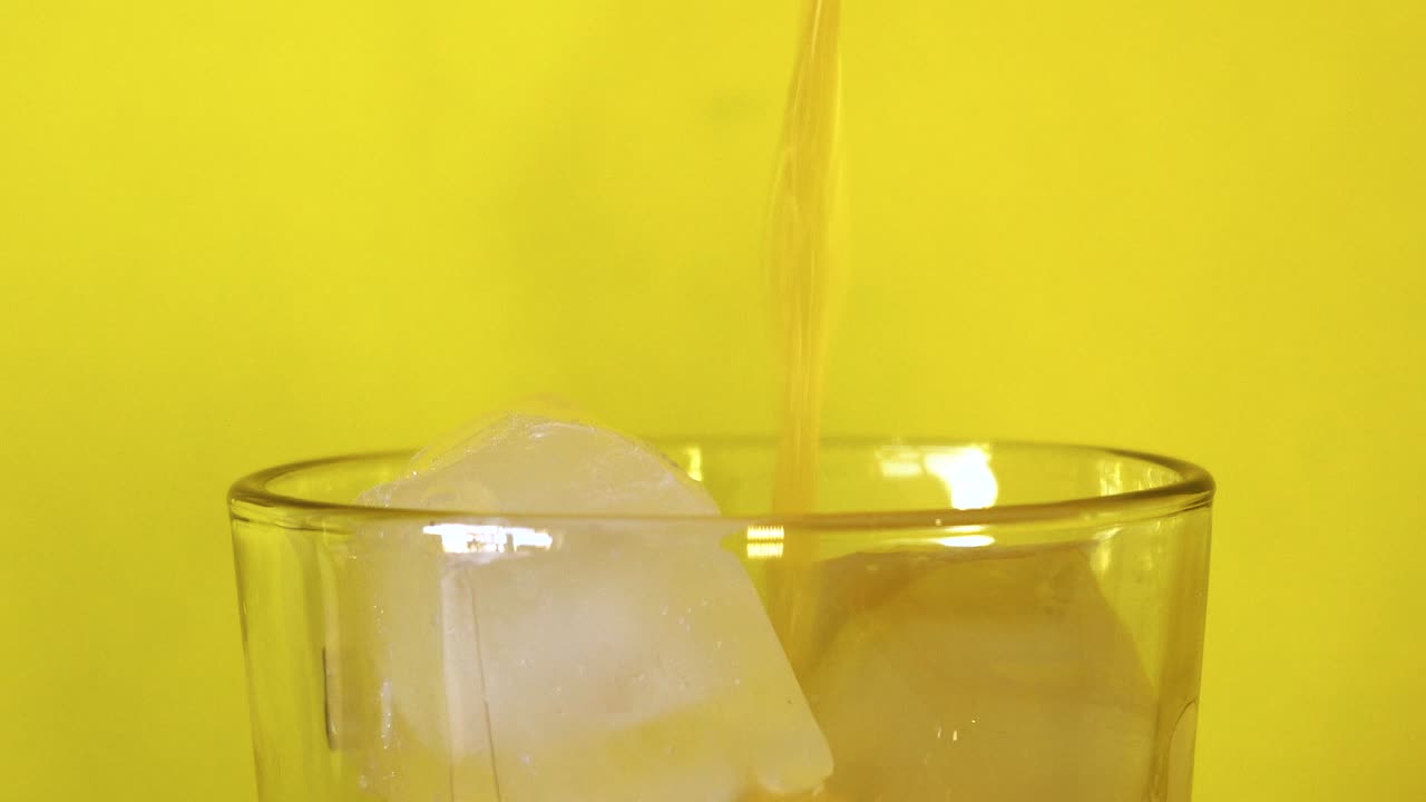 Pouring fresh orange juice into a glass with ice cubes