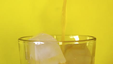 pouring fresh orange juice into a glass with ice cubes