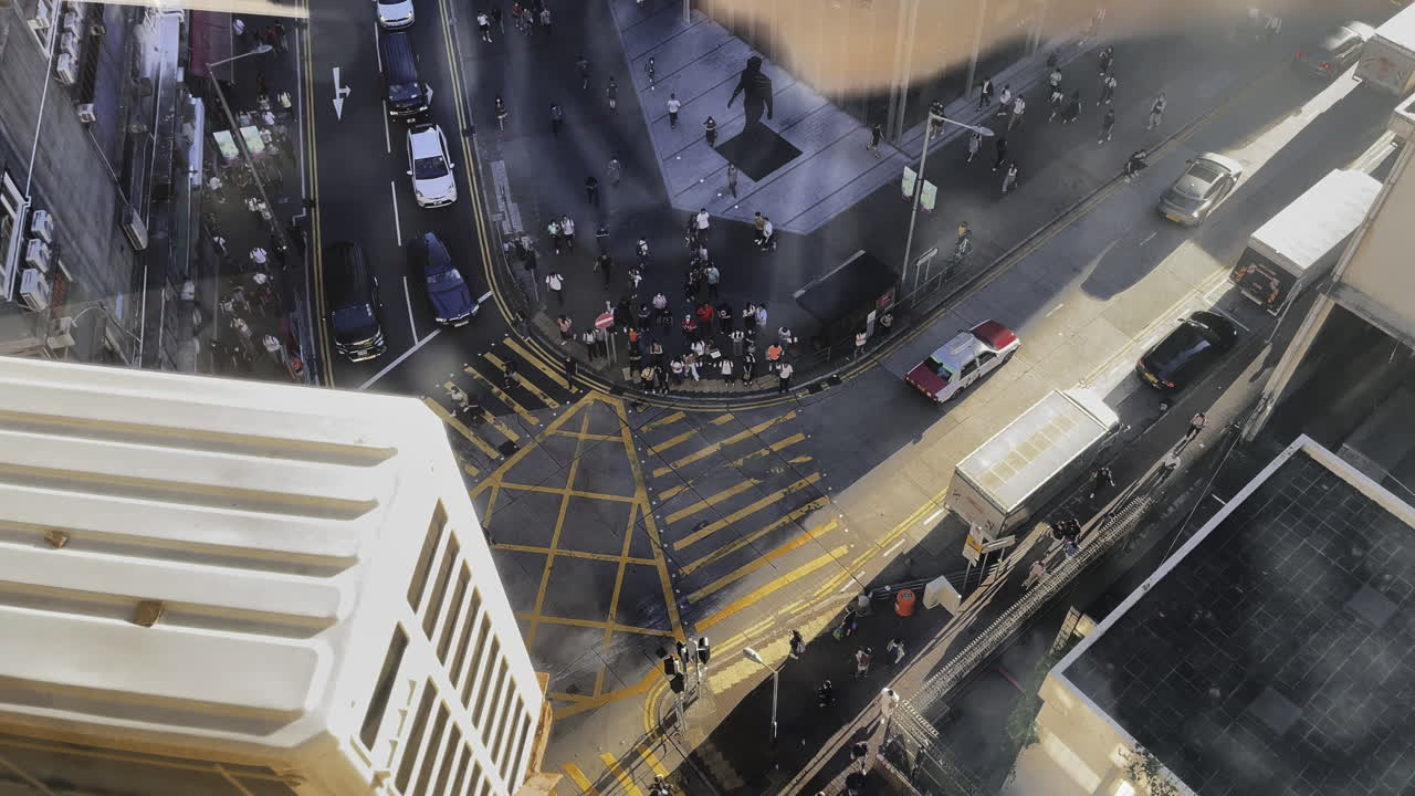 tomada aérea de arriba hacia abajo de un rascacielos que muestra una multitud de personas cruzando la carretera en la ciudad de hong kong en un día soleado