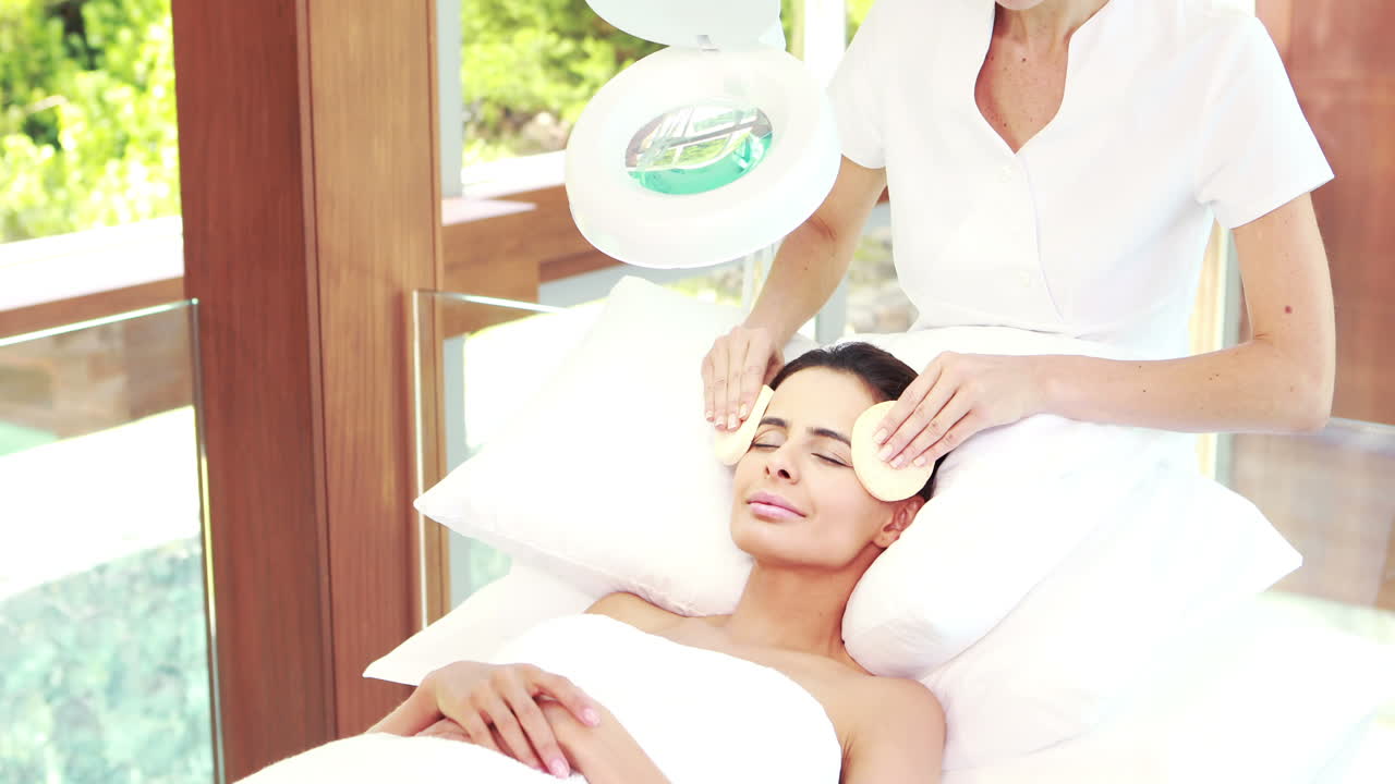 masajista limpiando la cara de la mujer con hisopos de algodón
