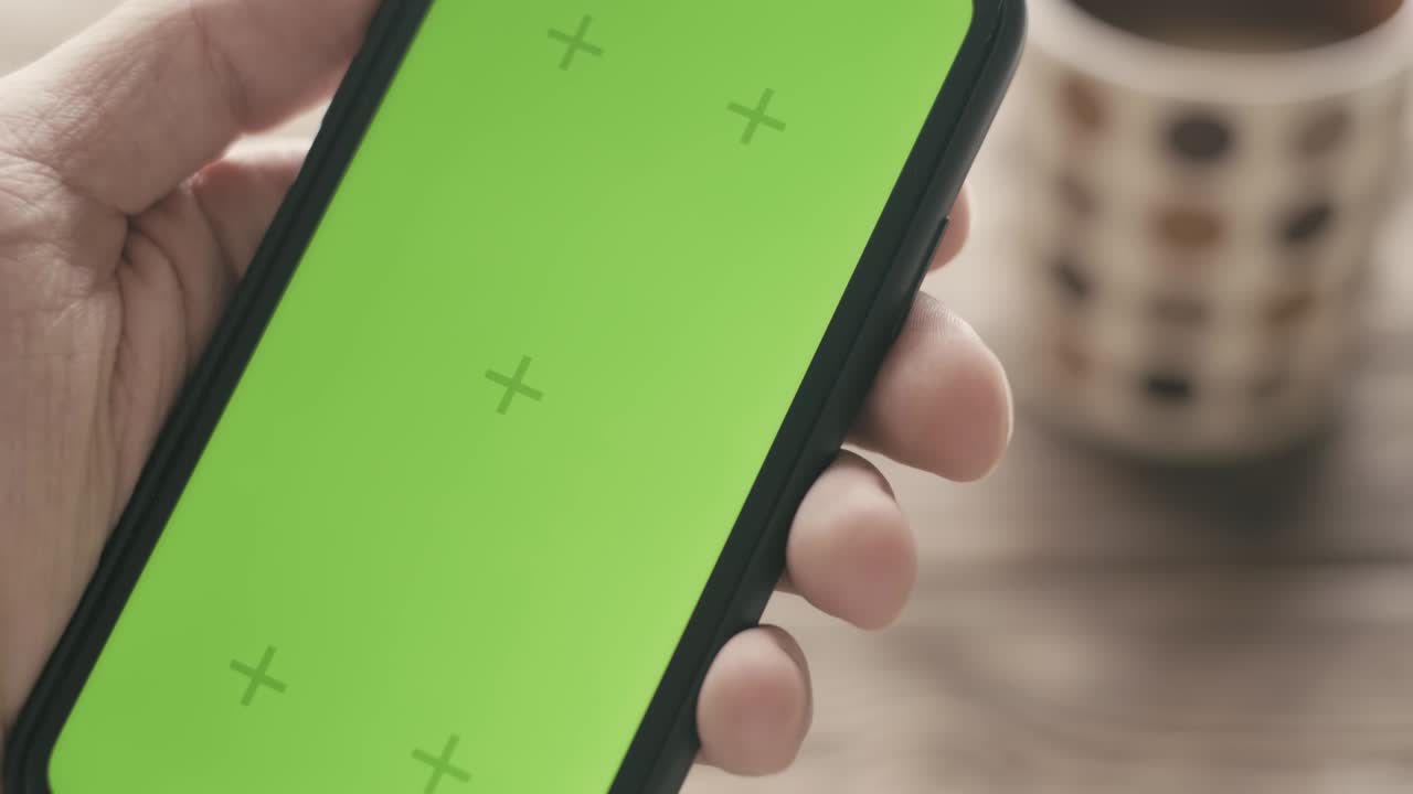 mano masculina sosteniendo un teléfono inteligente con pantalla verde.