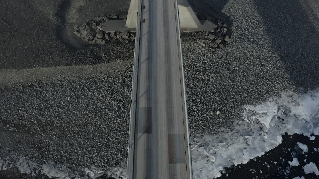 Birdseye view looking down at a bridge built over a black sand beach in Iceland