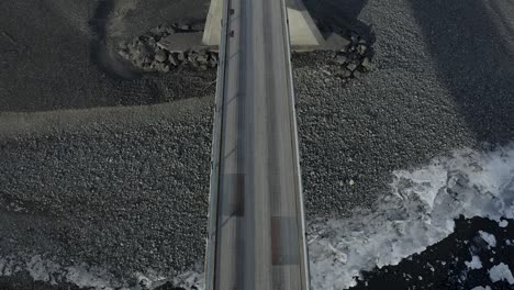 birdseye view looking down at a bridge built over a black sand beach in iceland