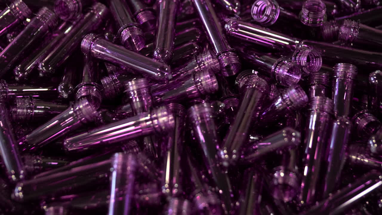 Gros plan sur des préformes de bouteilles en plastique violettes se déplaçant en vrac